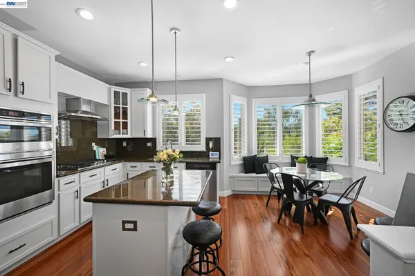 a kitchen with stainless steel appliances granite countertop a stove a refrigerator a kitchen island a dining table and chairs with wooden floor