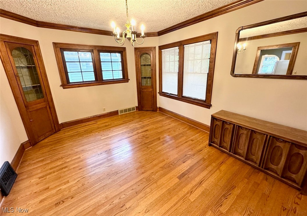 1011 Rushleigh Road Cleveland, OH 44121 - Photo 7 of 27 Spare room featuring light hardwood floors, a notable chandelier, a wealth of natural light, and a textured ceiling