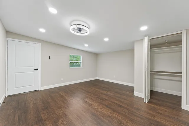 an empty room with wooden floor fan and windows