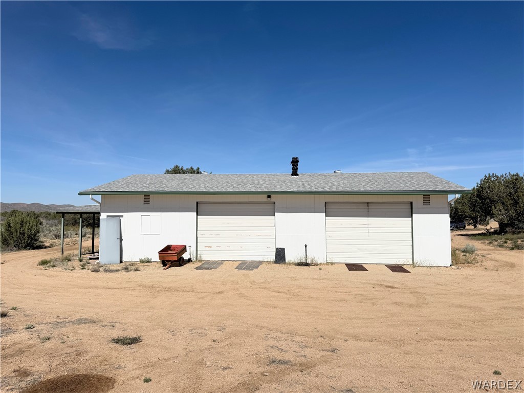 1575 South Roy Road Kingman, AZ 86401 - Photo 19 of 56 The property features a building with a light-colored exterior and a gray roof, equipped with two garage doors and an additional side entry door