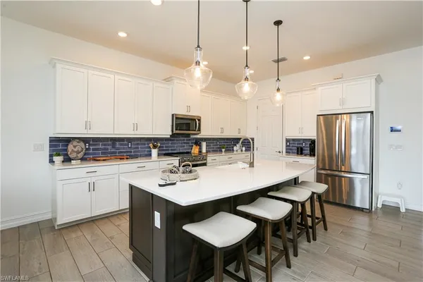 a kitchen with stainless steel appliances kitchen island granite countertop a sink a stove a refrigerator and white cabinets with wooden floor