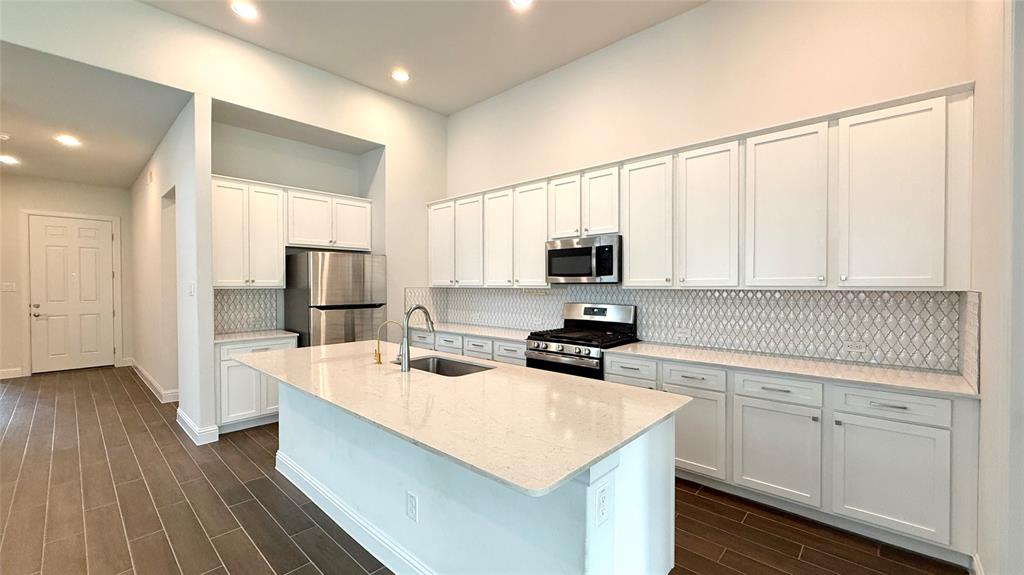 601 C-Bar Ranch Trail, Unit 27 Cedar Park, TX 78613 - Photo 5 of 29 Kitchen featuring a central island with an undermount sink, stainless steel appliances, white cabinetry, a tiled backsplash, and wood-finish flooring