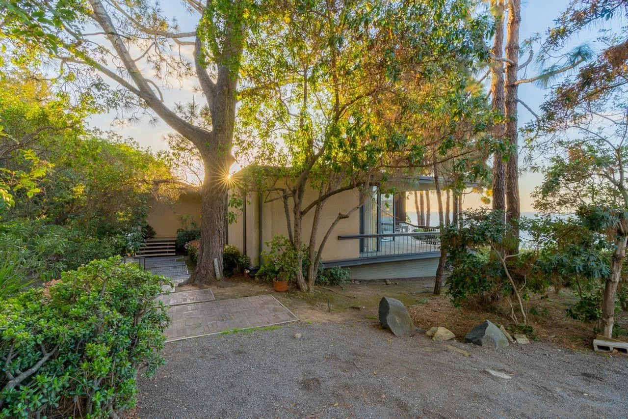 1595 Coast Walk La Jolla, CA 92037 - Photo 17 of 24 a view of a house with large trees and a bench