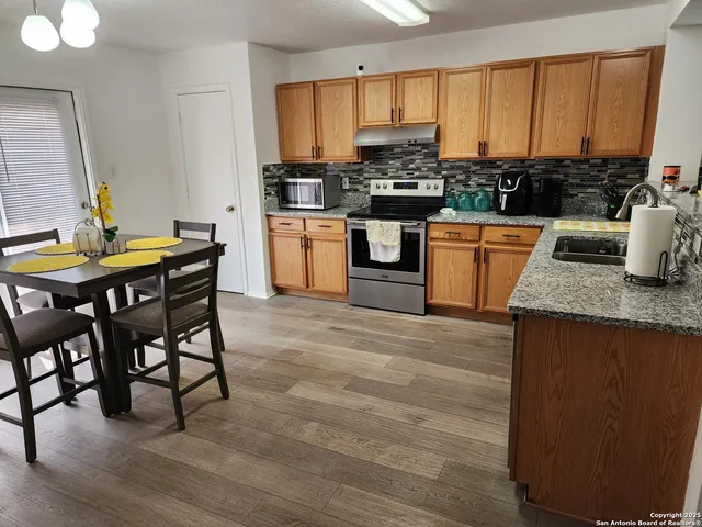 a kitchen with stainless steel appliances granite countertop a stove top oven a sink dishwasher a dining table and chairs with wooden floor