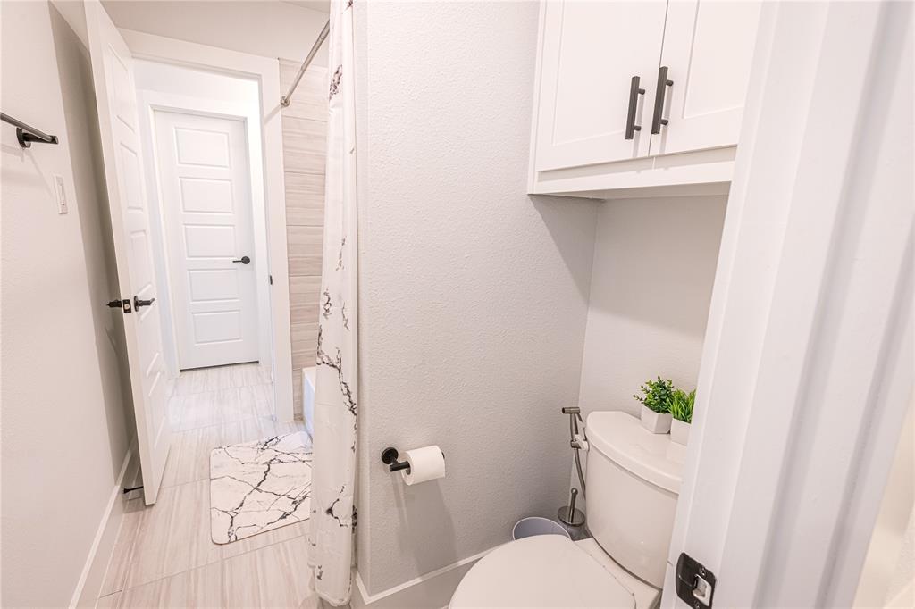 12135 Cotton Field Road Frisco, TX 75035 - Photo 33 of 38 Full bathroom featuring a white toilet with an overhead storage cabinet, a shower with a tiled surround, and light-toned tile flooring