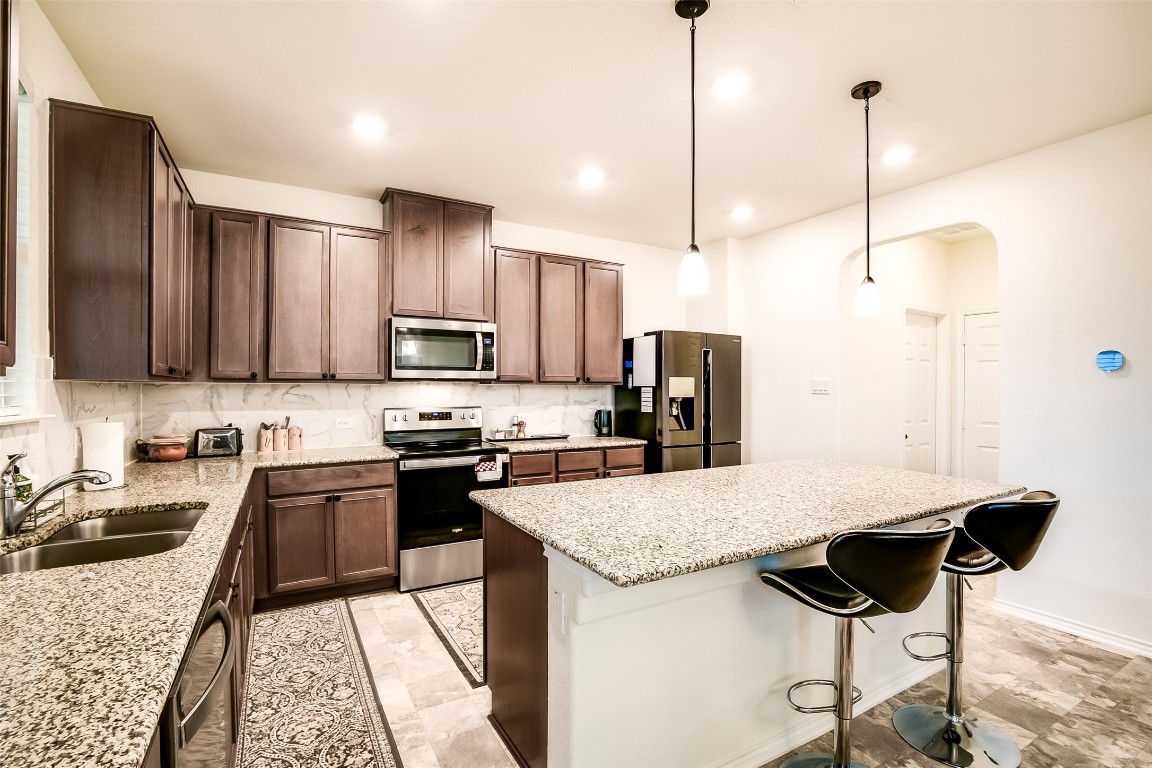 1924 Stringer Pass Leander, TX 78641 - Photo 16 of 34 a kitchen with stainless steel appliances kitchen island granite countertop a sink refrigerator and cabinets