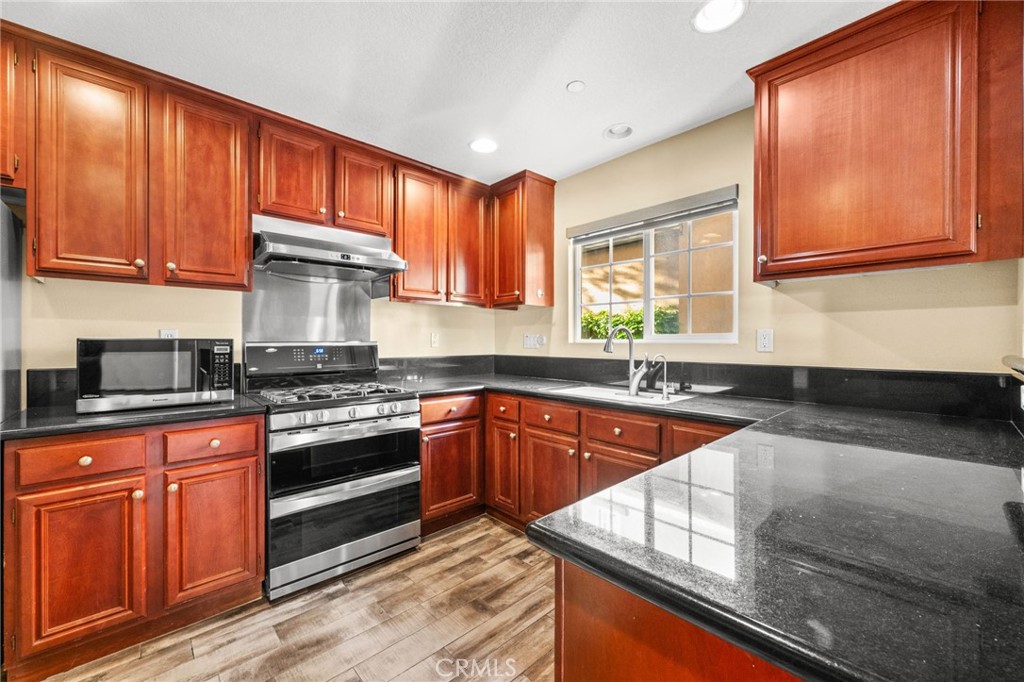 43 Three Vines Court Ladera Ranch, CA 92694 - Photo 14 of 42 a kitchen with stainless steel appliances granite countertop wooden cabinets a stove top oven a sink and dishwasher with wooden floor