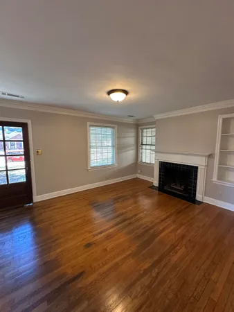 an empty room with wooden floor fireplace and windows
