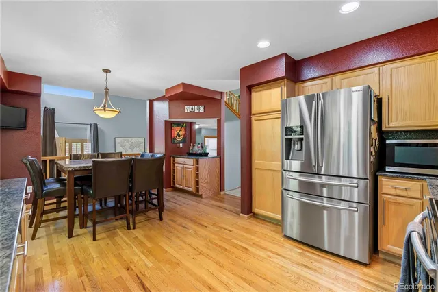 a kitchen with stainless steel appliances granite countertop a refrigerator a stove a dining table and chairs with wooden floor