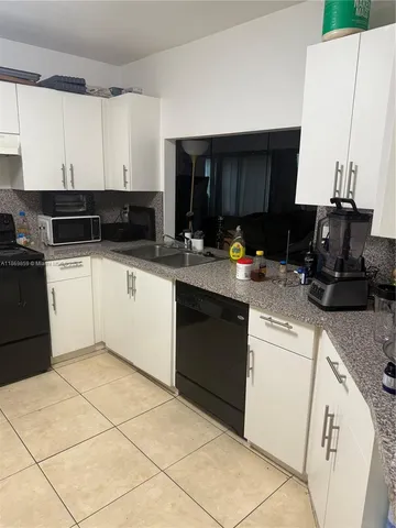 a kitchen with granite countertop a sink a stove top oven and white cabinets
