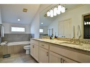 a bathroom with a double vanity sink a toilet a mirror and bathtub