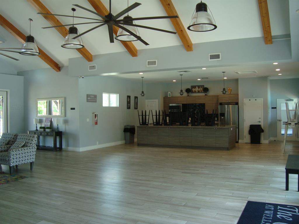 814 Broken Feather Trail Pflugerville, TX 78660 - Photo 23 of 24 The expansive common room features exposed beam ceilings and light-toned hardwood-style flooring, creating an inviting space for community gatherings.