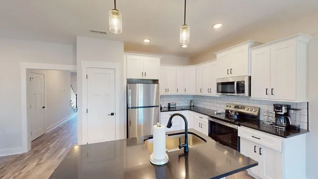 a kitchen with granite countertop a refrigerator a stove a sink and white cabinets with wooden floor