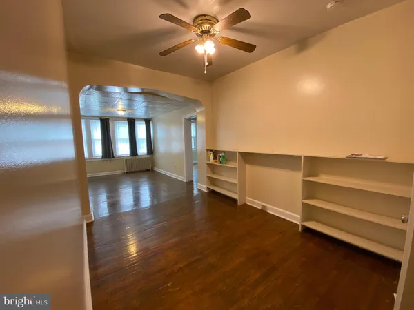 a view of an empty room with chandelier fan and wooden floor