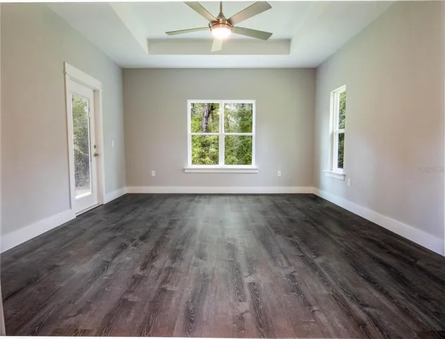 an empty room with wooden floor chandelier fan and windows
