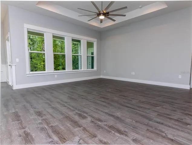 an empty room with wooden floor fan and windows