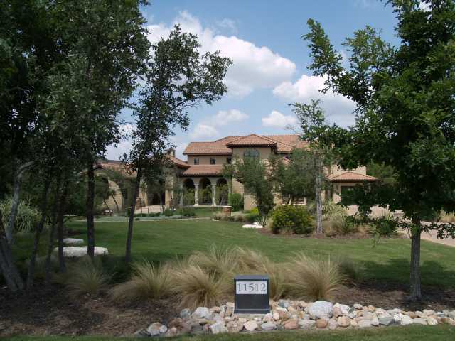 a view of a white house with a big yard and potted plants and large trees