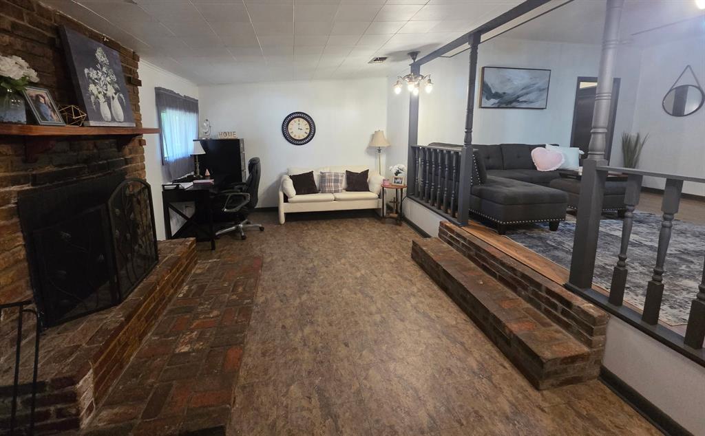 301 Old Plain Dealing Road Benton, LA 71006 - Photo 5 of 19 Spacious living area featuring wood-finish flooring, a prominent brick fireplace with a wood mantle, and a partial dark wood baluster railing separating areas