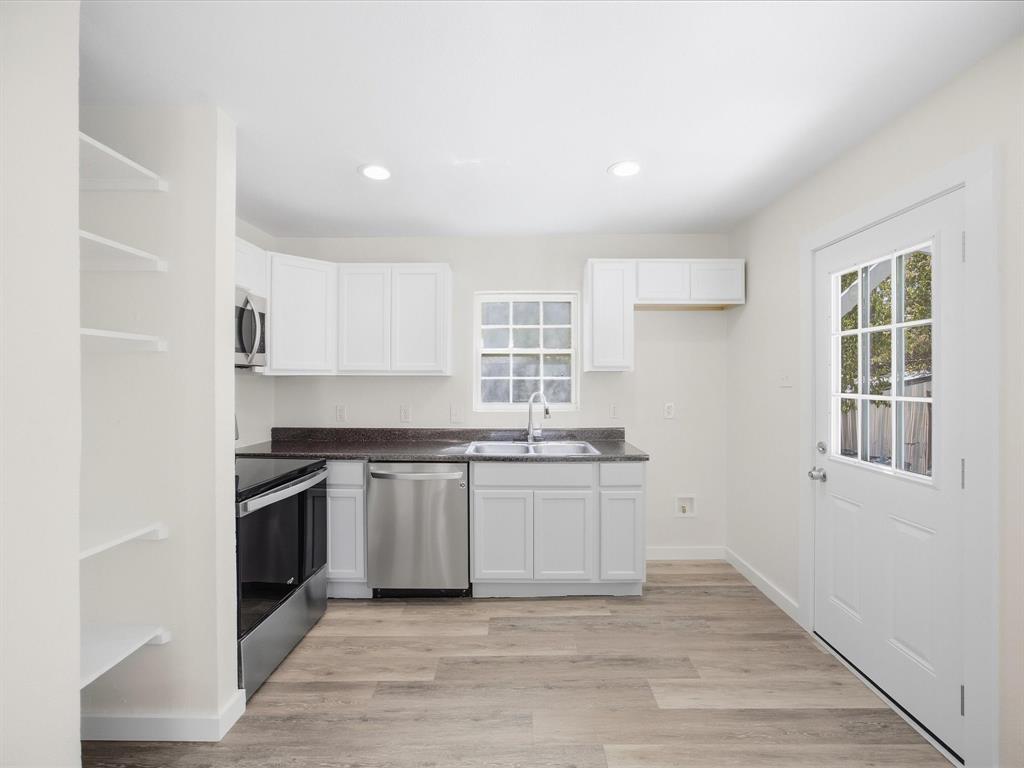 6933 Hatch Road Lake Worth, TX 76135 - Photo 13 of 28 Kitchen featuring white cabinetry, dark countertops, stainless steel appliances, wood-finish flooring, and a glass-paned door