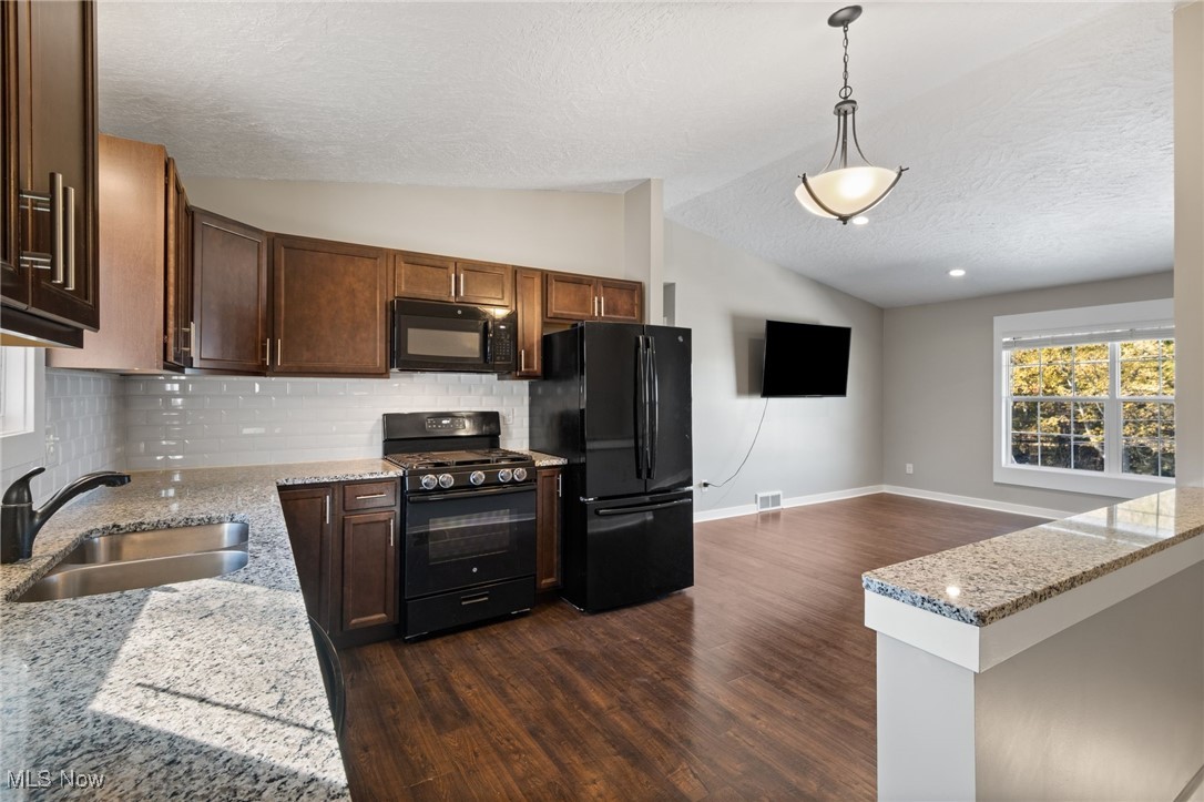 3213-3217 Pickle Road Green, OH 44312 - Photo 10 of 41 Kitchen with light stone countertops, black appliances, vaulted ceiling, decorative backsplash, and dark wood-style flooring