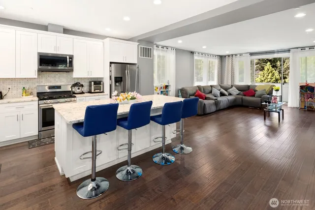 a kitchen with stainless steel appliances granite countertop a refrigerator a stove a sink dishwasher and a dining table with wooden floor