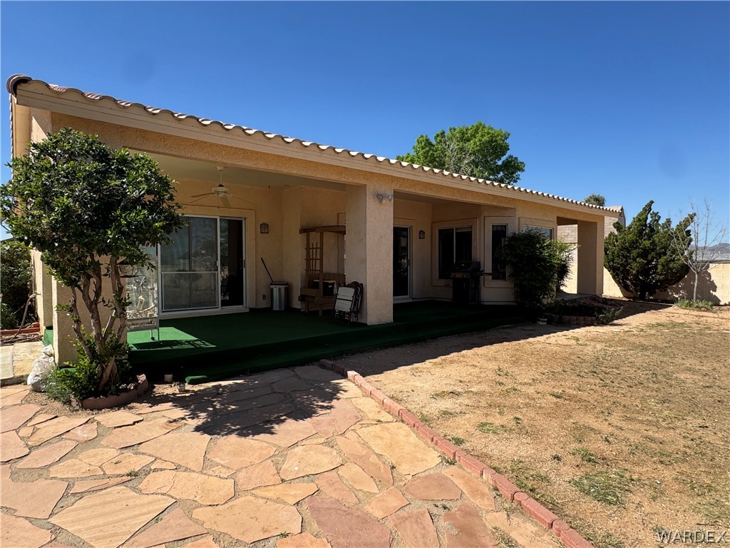 4029 Roma Road Kingman, AZ 86401 - Photo 51 of 90 The property features a covered patio with a ceiling fan and sliding glass doors, overlooking a yard with a flagstone path and mature trees
