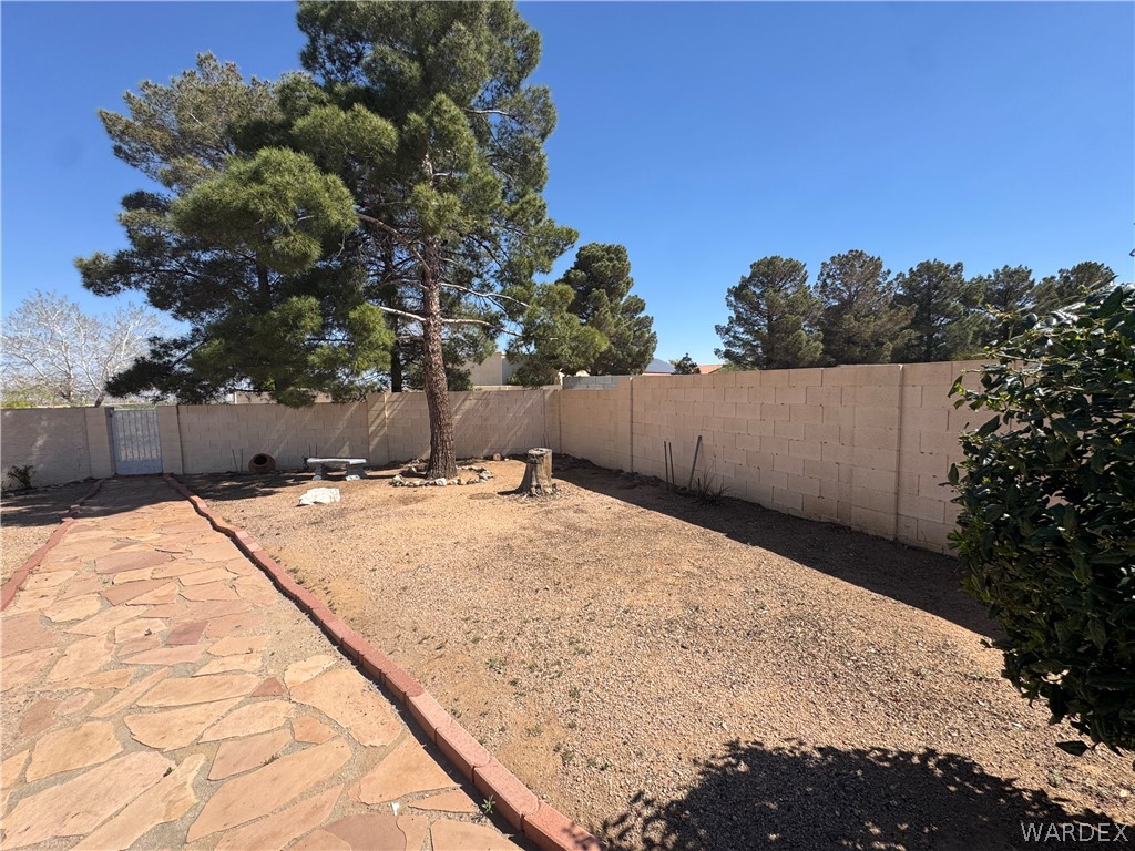 4029 Roma Road Kingman, AZ 86401 - Photo 56 of 90 The property features a spacious yard with a stone pathway, a mature tree, and a block wall perimeter