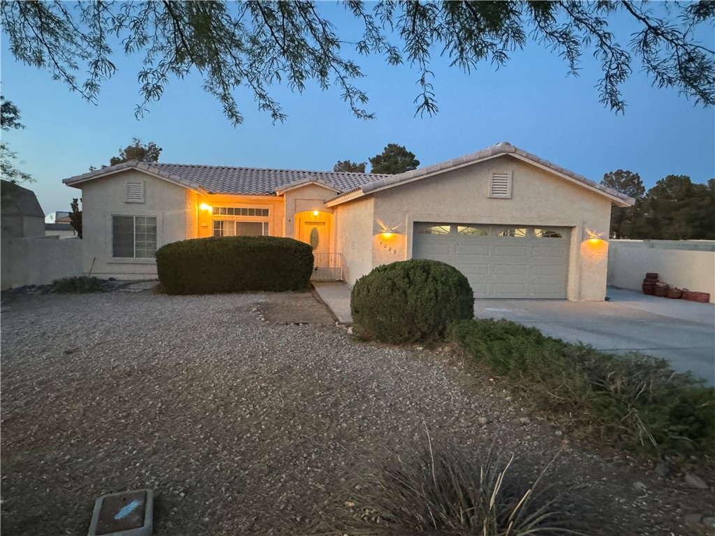 4029 Roma Road Kingman, AZ 86401 - Photo 80 of 90 The property features an attached garage with a paved driveway, front landscaping with decorative rocks, and exterior lighting illuminating the facade