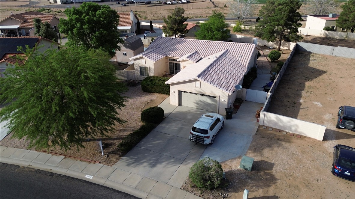 4029 Roma Road Kingman, AZ 86401 - Photo 85 of 90 The property features a concrete driveway leading to an attached garage, a mature tree in the front yard, and a fenced side yard with exposed earth