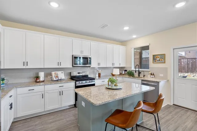 a kitchen with stainless steel appliances kitchen island granite countertop a sink a stove white cabinets with wooden floor and cabinets