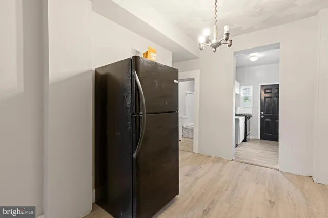 a view of a refrigerator in kitchen and an empty room with wooden floor