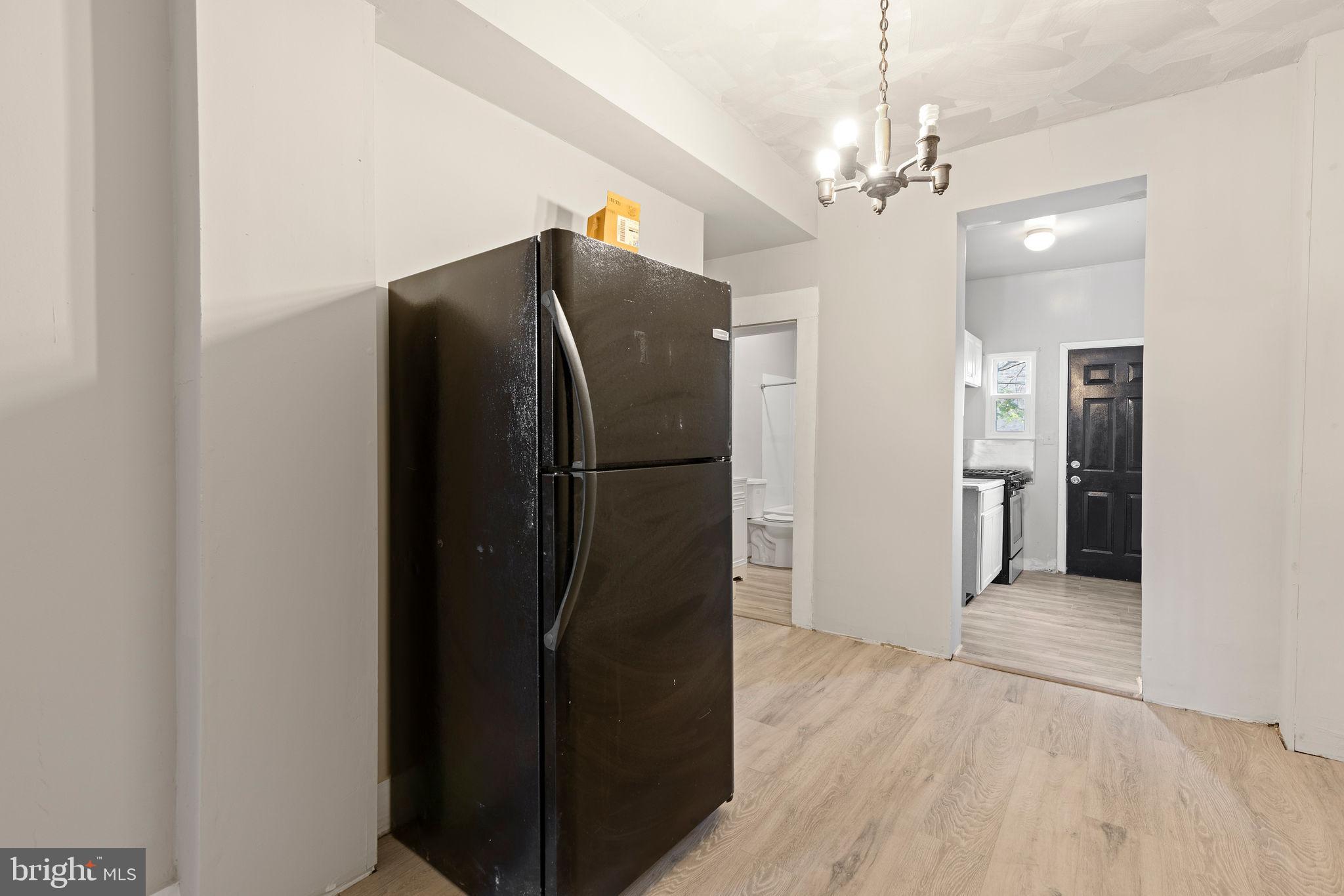 3003 Clifton Avenue Baltimore, MD 21216 - Photo 8 of 28 a view of a refrigerator in kitchen and an empty room with wooden floor