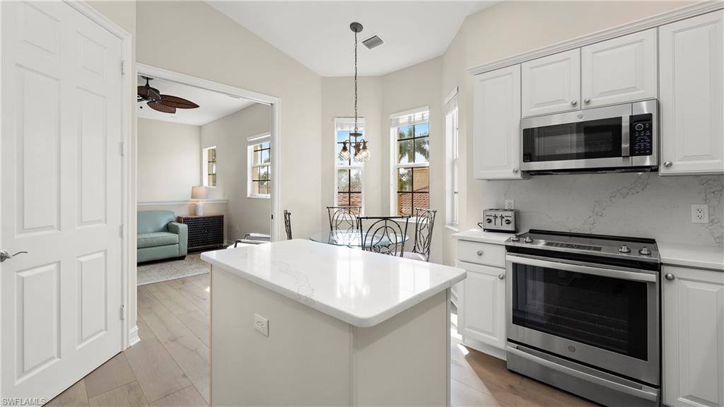 8617 Champions Point, Unit 403 Naples, FL 34113 - Photo 7 of 37 Kitchen featuring stainless steel appliances, white cabinets, pendant lighting, a kitchen island, and vaulted ceiling