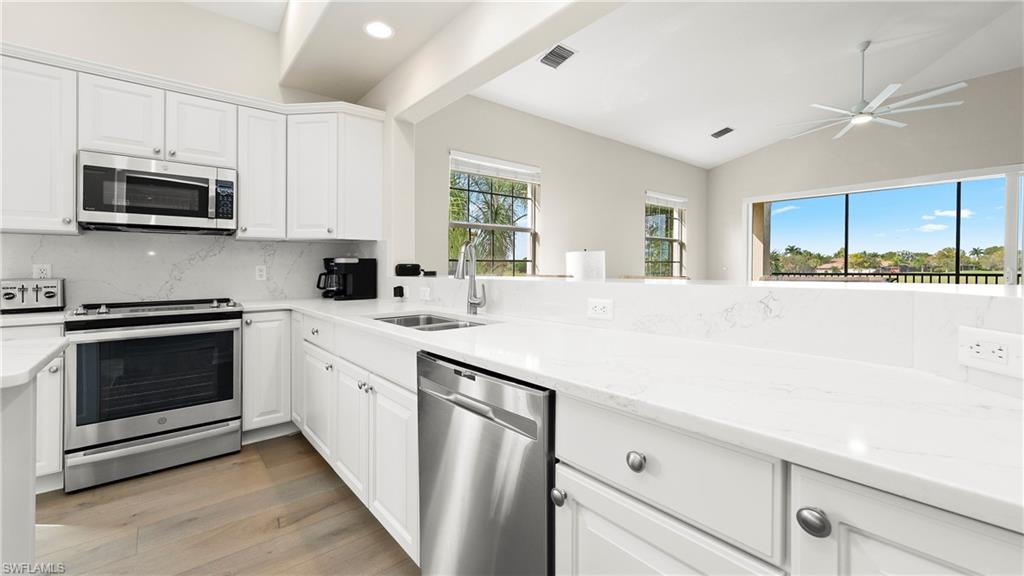 8617 Champions Point, Unit 403 Naples, FL 34113 - Photo 8 of 37 Kitchen featuring appliances with stainless steel finishes, white cabinetry, lofted ceiling, light stone counters, and backsplash