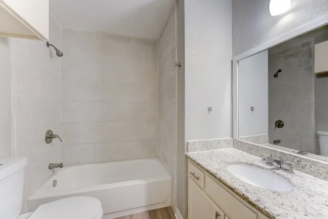 a bathroom with a granite countertop tub sink toilet and mirror
