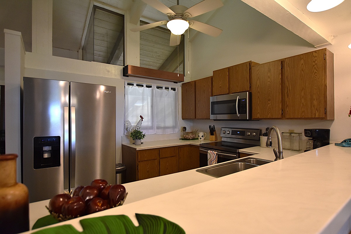 68-3840 Lua Kula Street, Unit D203 Waikoloa, HI 96738 - Photo 7 of 30 a kitchen with stainless steel appliances kitchen island granite countertop a refrigerator a sink dishwasher a stove and a dining table with wooden floor