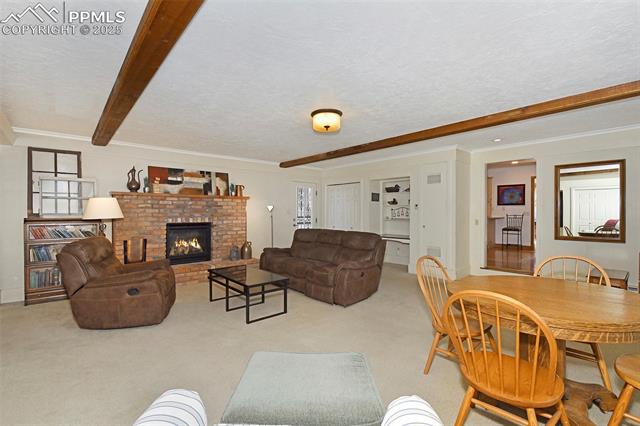2421 Strickler Road Colorado Springs, CO 80906 - Photo 22 of 44 Carpeted living area featuring a fireplace, a textured ceiling, crown molding, and beam ceiling