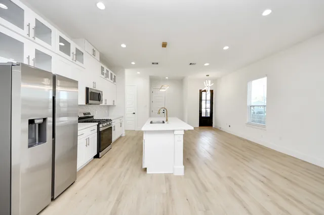 a kitchen with stainless steel appliances kitchen island granite countertop a stove a sink and white cabinets with wooden floor