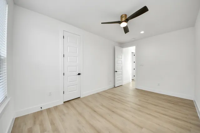 an empty room with wooden floor ceiling fan and window