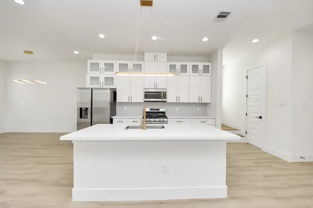 a large white kitchen with stainless steel appliances granite countertop a refrigerator oven a sink dishwasher and white cabinets with wooden floor