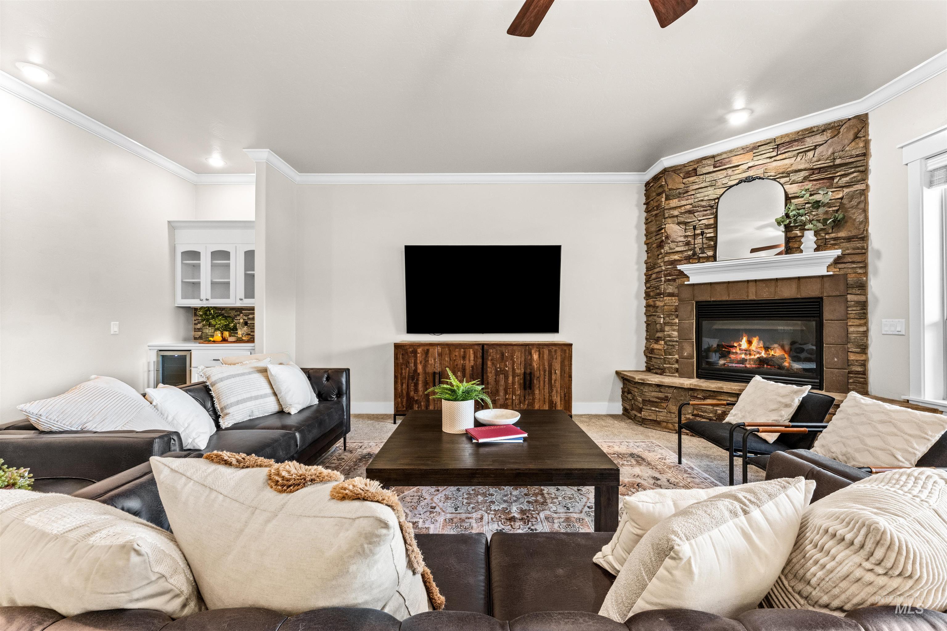 1177 East Riversong Drive Eagle, ID 83616 - Photo 11 of 36 Living room with a stone fireplace, ceiling fan, crown molding, and a dry bar