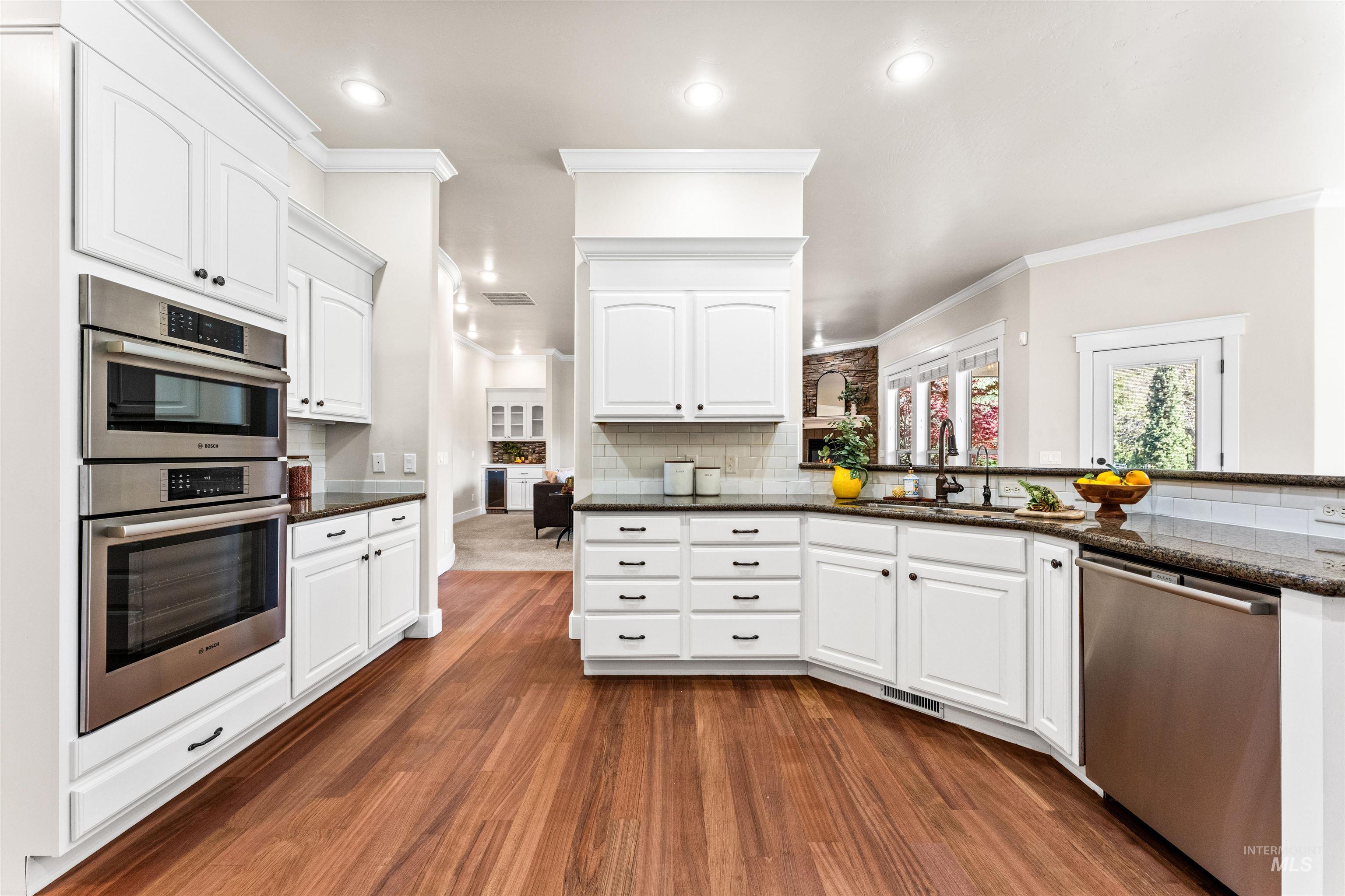 1177 East Riversong Drive Eagle, ID 83616 - Photo 6 of 36 Kitchen with dark stone counters, stainless steel appliances, white cabinetry, tasteful backsplash, and dark wood-style floors