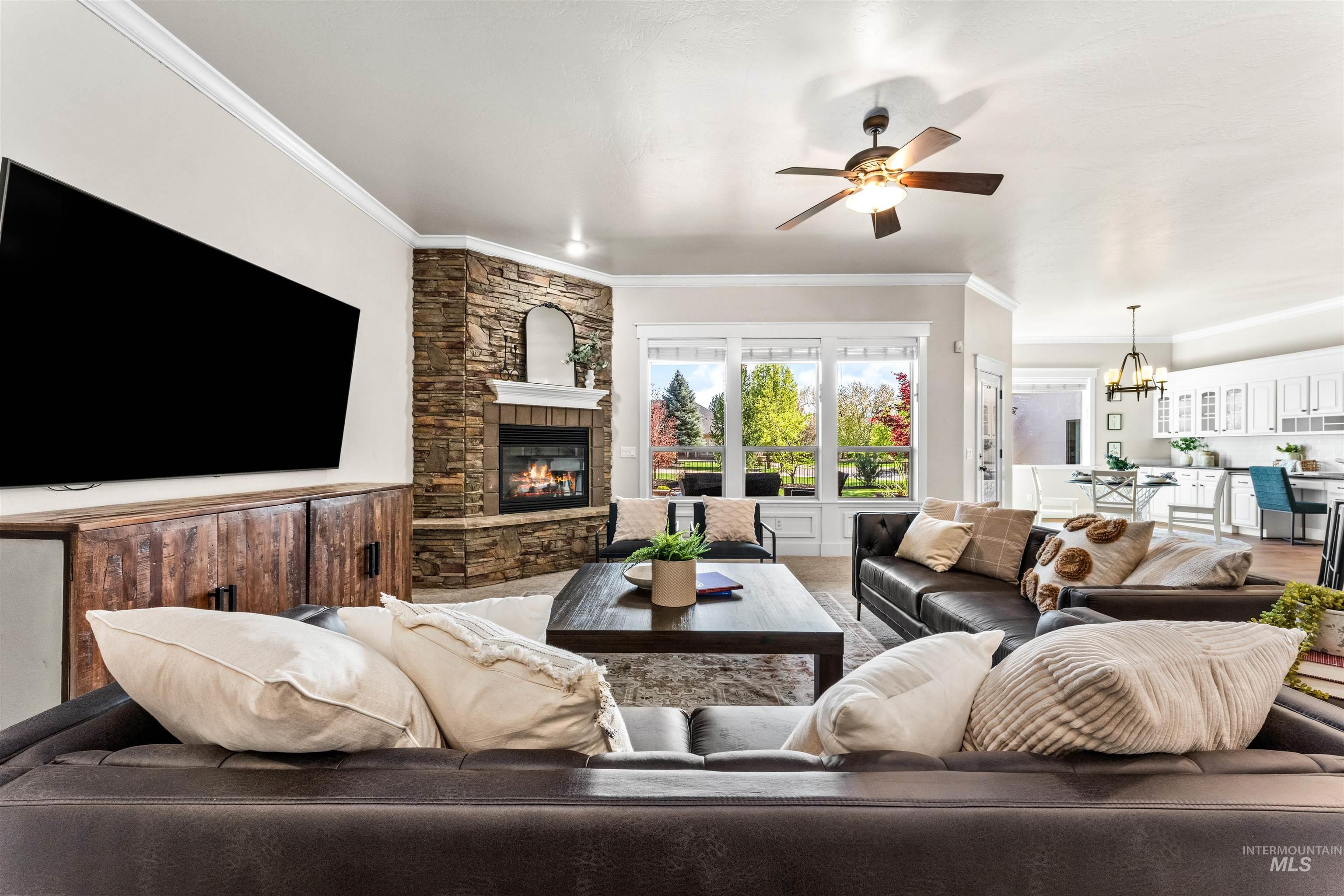 1177 East Riversong Drive Eagle, ID 83616 - Photo 10 of 36 Living area featuring a ceiling fan, a fireplace, a chandelier, ornamental molding, and wainscoting