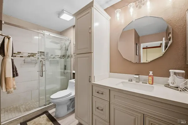 a bathroom with a toilet a sink a glass door a shower a mirror and vanity