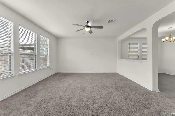 an empty room with chandelier fan and windows