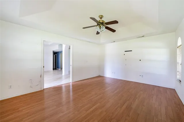 a view of an empty room with wooden floor and a ceiling fan