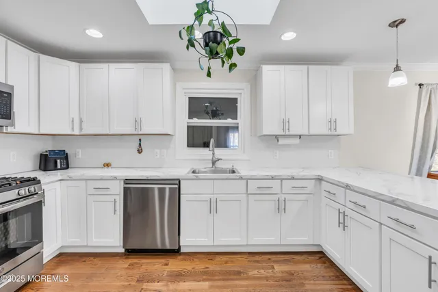 a kitchen with stainless steel appliances granite countertop a sink a stove a microwave a refrigerator a white cabinets and wooden floor