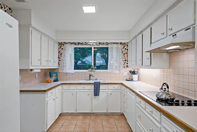 a kitchen with a sink dishwasher a stove and white cabinets