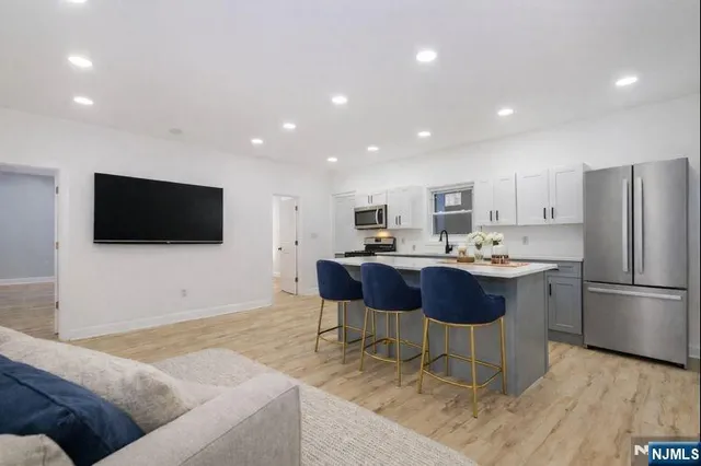 a living room with stainless steel appliances furniture a flat screen tv and kitchen view