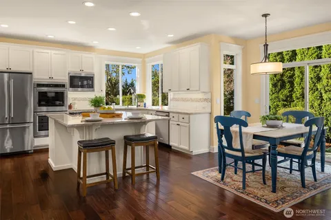 a kitchen with stainless steel appliances granite countertop a stove a refrigerator a kitchen island a dining table and chairs with wooden floor